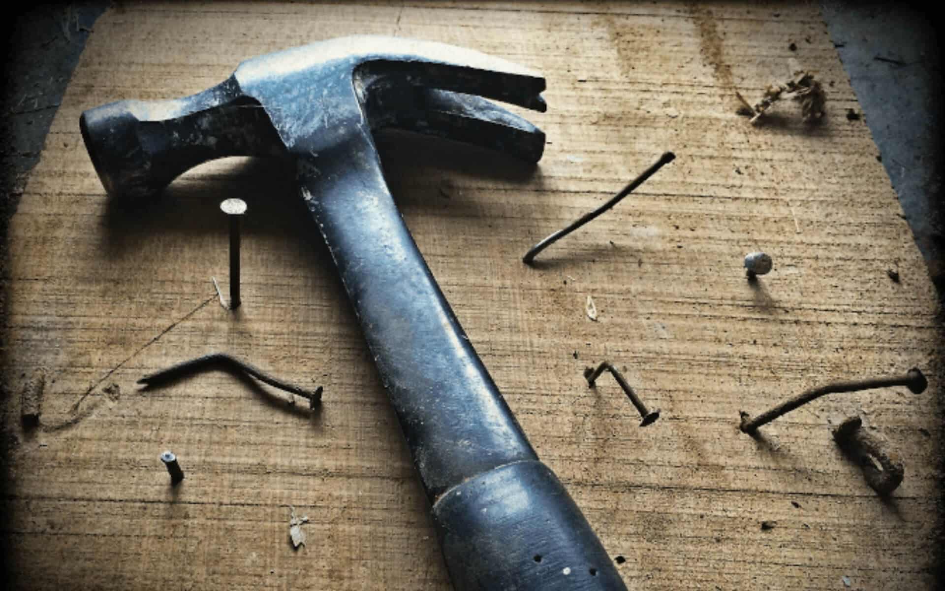 A hammer lies among a bunch of bent nails and one straight one half hammered